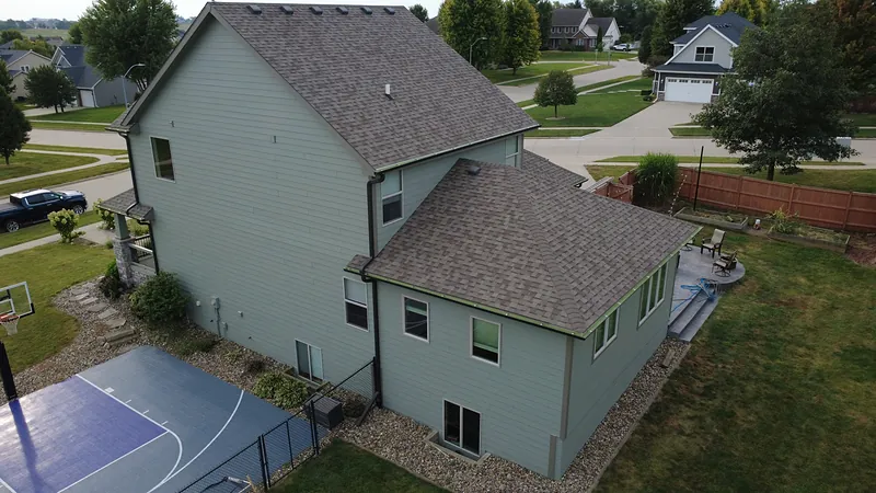 Aerial view of the side and rear of a pale green Waukee home with stone accents after exterior painting by Mission Painting